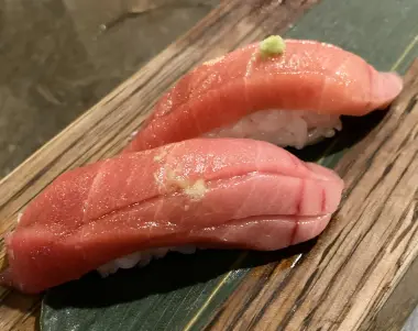two pieces of tuna sushi served on a banana leaf, with a small bit of wasabi on top